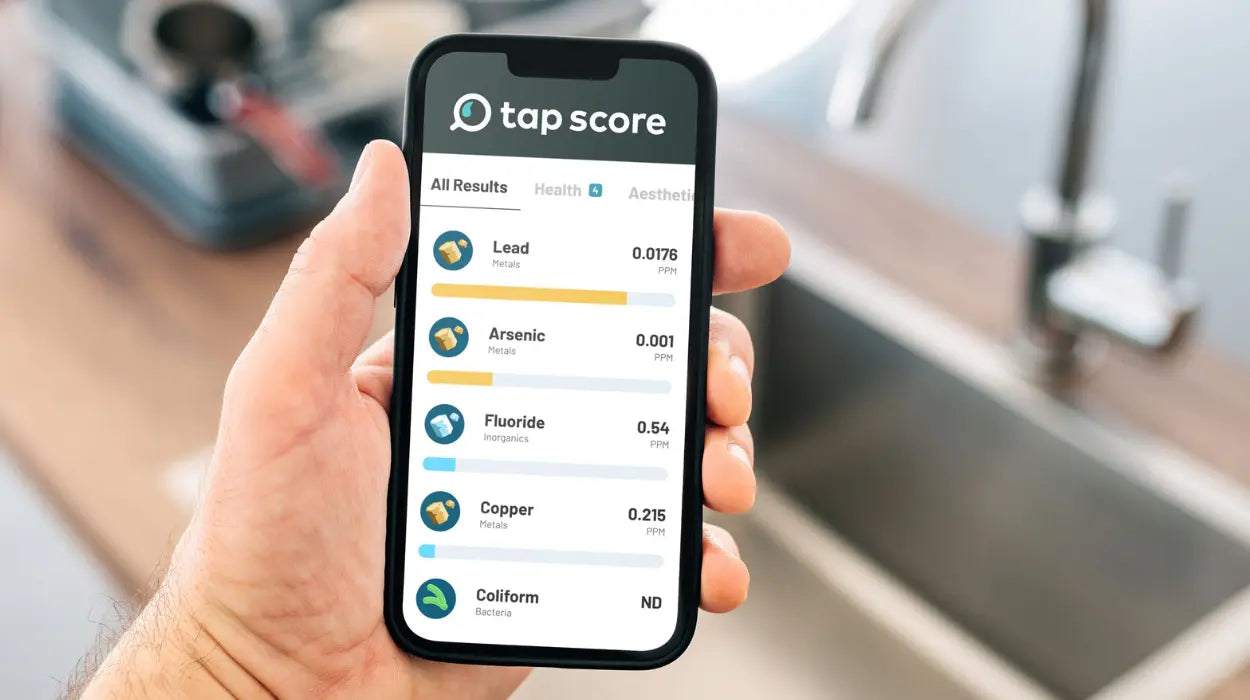Hand holding a smartphone displaying the 'tap score' app with water quality results in a kitchen setting.